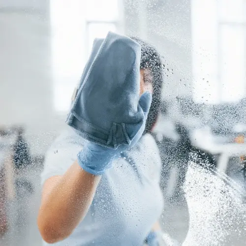 Professional cleaner wiping down a glass window, showcasing thorough cleaning services.